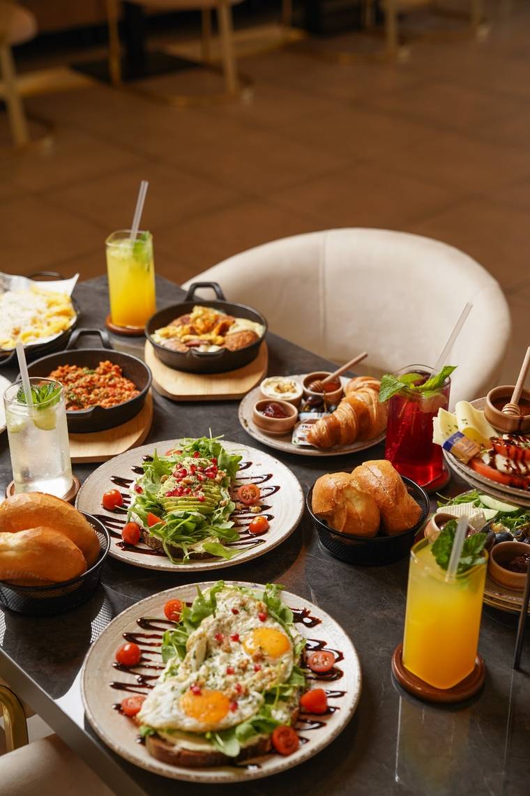 Reich gedeckter Frühstückstisch mit Avocadobrot, Eiergerichten, Croissants und frischen Säften