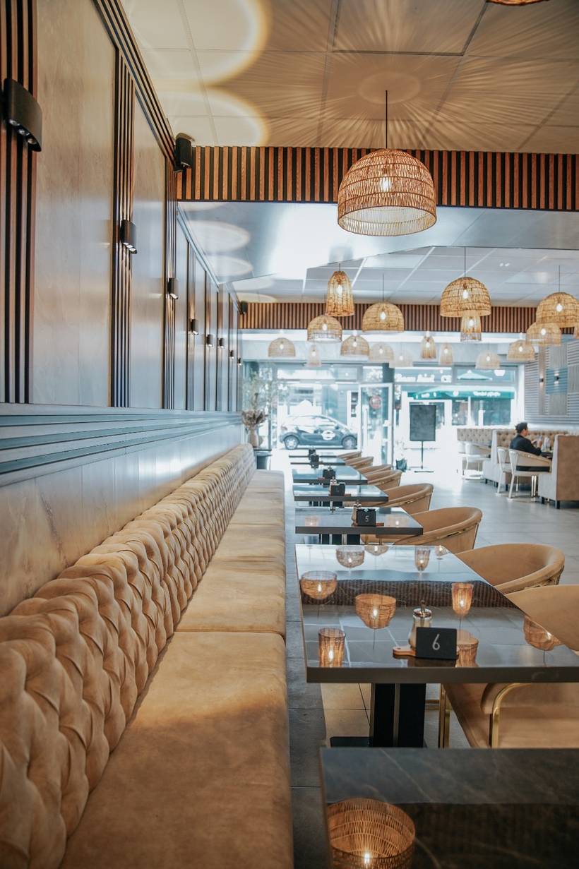 Blick in das Ceyse Cafe: lange Sitzbank in Sandbeige, Rattanlampen und dunkle Holzlamellen