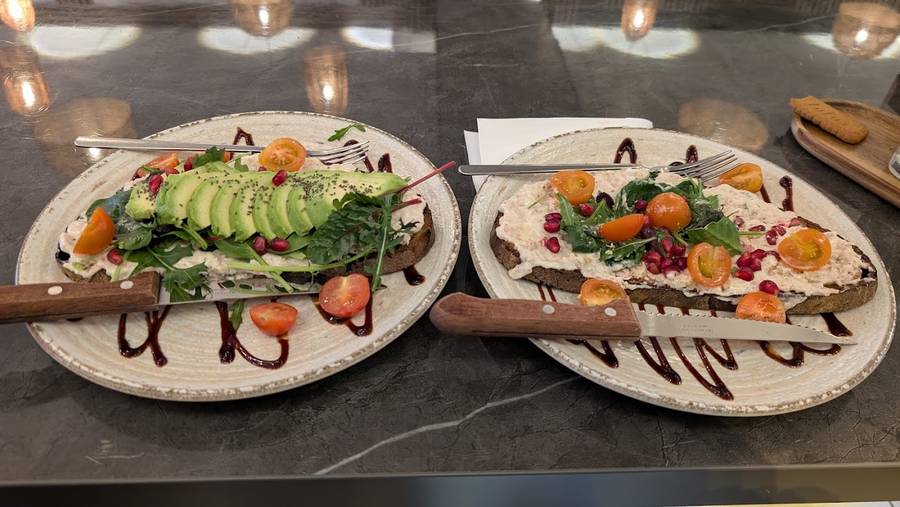Zwei belegte Brote mit Avocado, Granatapfel und Kirschtomaten auf Steinguttellern